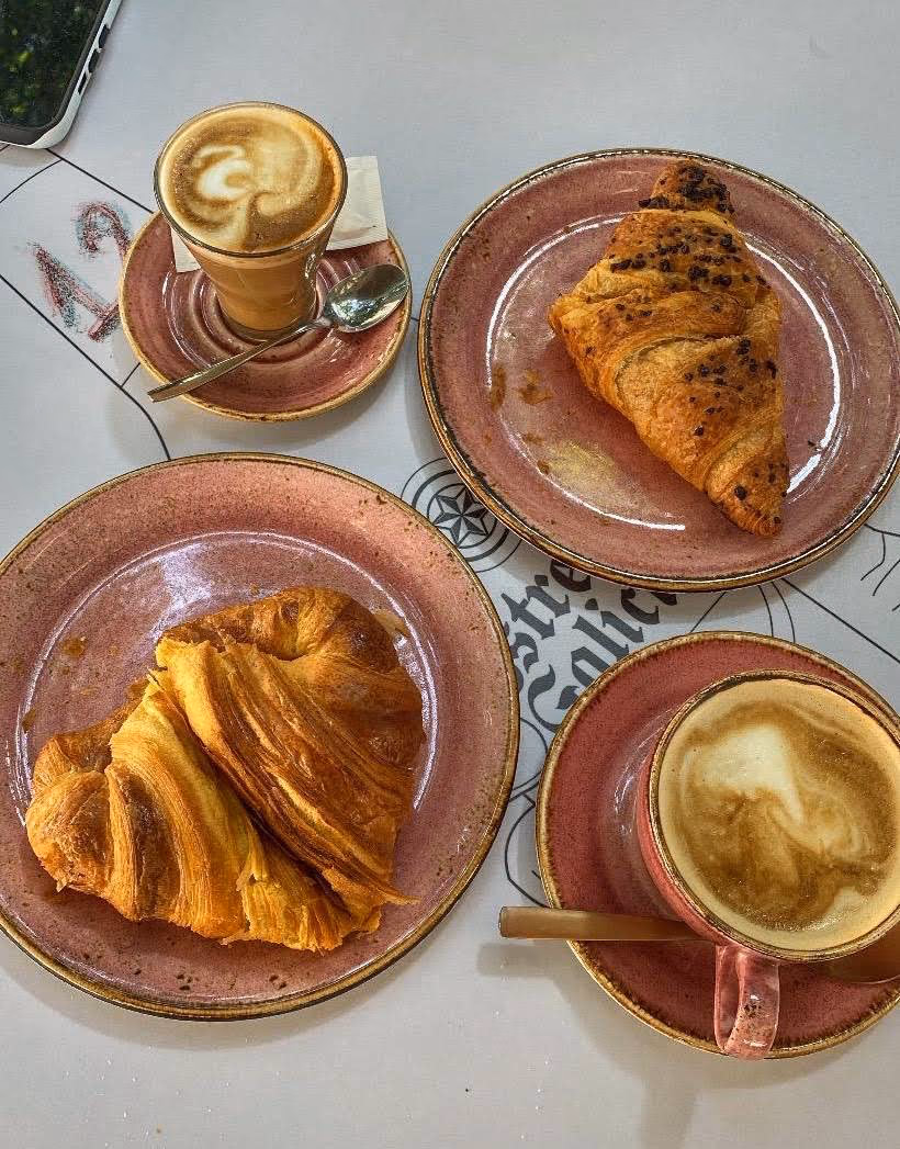 Mesa con café con leche, croissant de hojaldre y pastel recién servidos en La Caprichosa